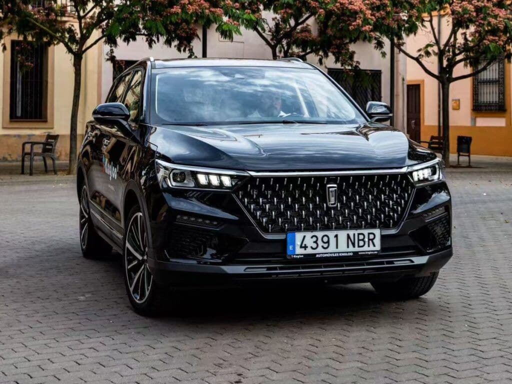 SUV negro brillante estacionado en una calle empedrada con árboles de flores rosas al fondo.