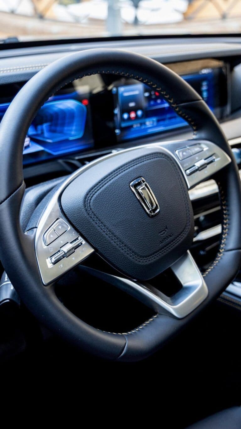 Volante de cuero negro con controles plateados y tablero digital con pantallas de color azul.