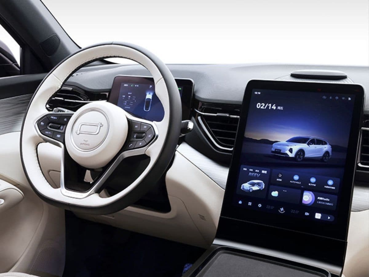 Interior de coche moderno con volante bicolor, panel digital y gran pantalla táctil vertical central.