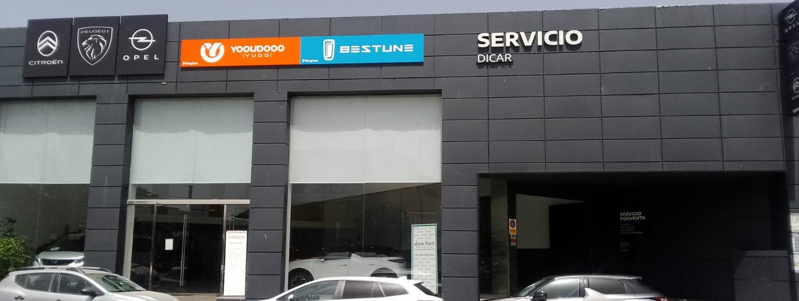 Fachada de concesionario con logotipos de Citroën, Peugeot, Opel, Yudo y Bestune en edificio gris.